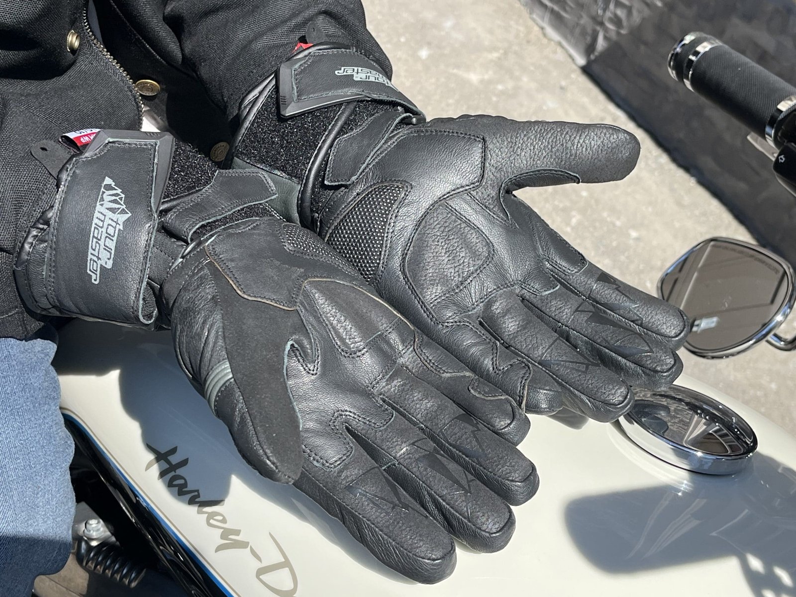 a motorcycle rider showing off the palms of the TOURMASTER Super Warm Waterproof Gloves on top of his harley davidson tank.