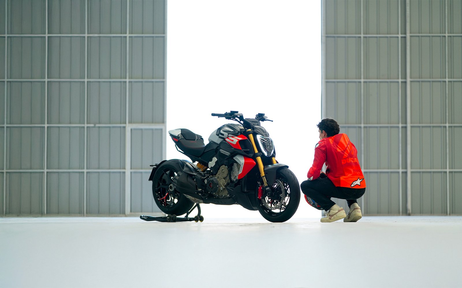 A side view of a Ducati Diavel V4 RS next to Marc Marquez