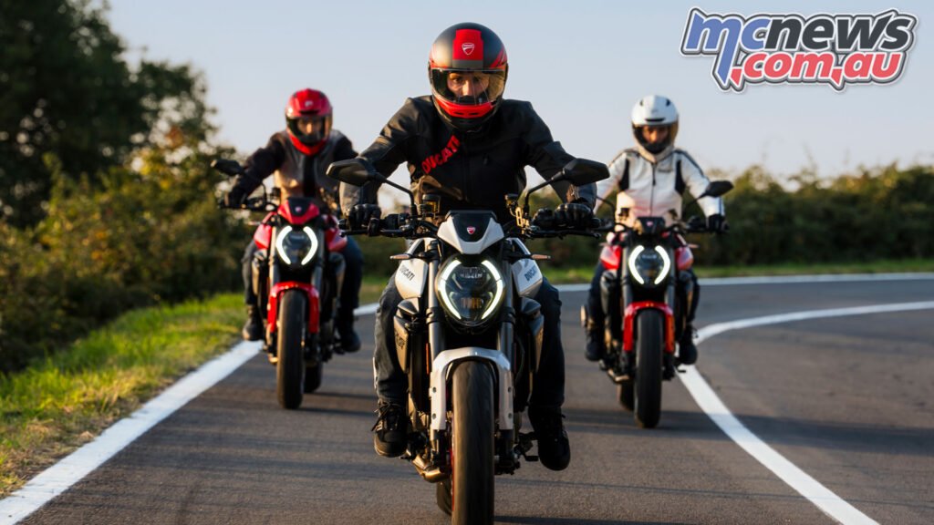 Rider on the 2026 Ducati Monster cornering on a public road, showing revised riding position and daytime running light.
