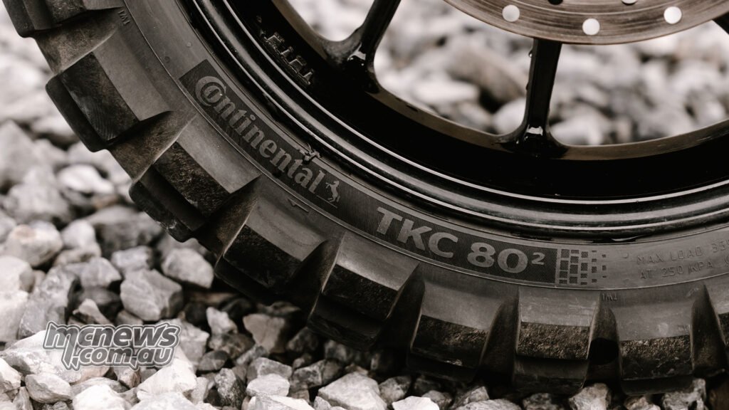 Close-up of Continental TKC 80² sidewall lettering beside a black alloy wheel on loose rocks.