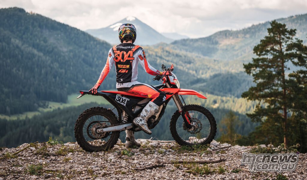 Rear three-quarter view of a rider on the 2027 KTM Freeride E at a rocky mountain viewpoint.